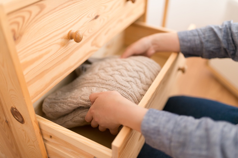 厚手のセーターを木のタンスにしまう女性